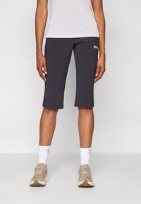 Grå treningsshorts til knærne i lett materiale, med en tettsittende design, diskret logodetalj, og kombinert med lyse joggesko og hvite sokker.