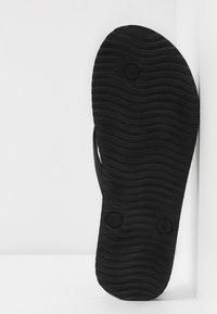 Black flip-flop sole with wavy texture, circular button accents, and a minimalist design, appearing on a white background.