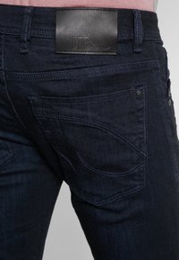 Jeans de mezclilla azul oscuro con una etiqueta de cuero LTB en la cinturilla, con costuras distintivas en los bolsillos traseros y una textura suave.