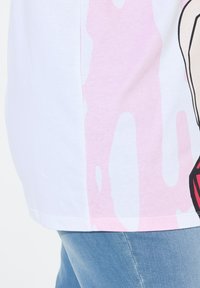 Hvid t-shirt med et stort pink grafisk design, korte ærmer og en afslappet pasform, parret med lyseblå denimjeans.
