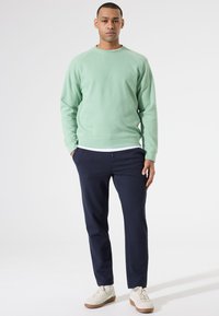Lichtgroene sweatshirt met een ronde halslijn en geribde mouwen, gecombineerd met marineblauwe joggingsbroeken en crèmekleurige sneakers.