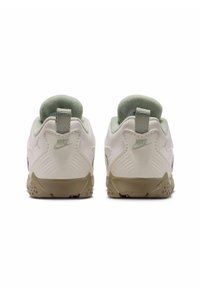 Białe sportowe sneakersy z zielonymi akcentami, wyściełanym obcasem, teksturowanymi bokami oraz detalem logo z tyłu. Okrągły kształt i gumowa podeszwa.