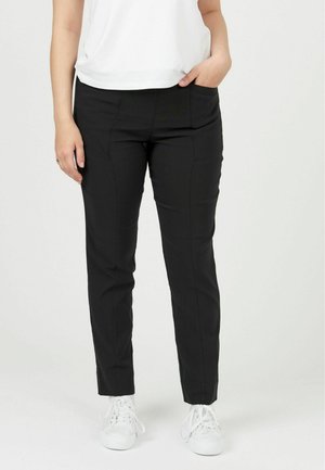 Čierne elastické nohavice s hladkým povrchom, slim fit strih, bočné vrecká, skombinované s bielymi teniskami a voľným bielym topom.