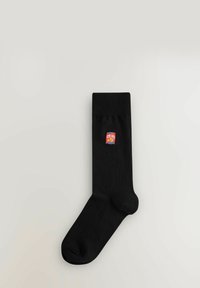 Sort bomuldsstr�ømpe med ribbet manchet og et lille rød og gult "CRISPS" logo patch på siden. Glat tekstur, standard strømpeform.