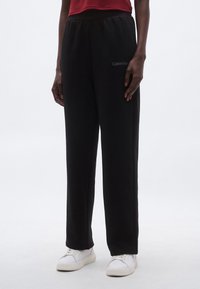 Czarne spodnie dresowe z miękkiego materiału o luźnym kroju, z elastycznym pasem i logo Calvin Klein po lewej stronie.