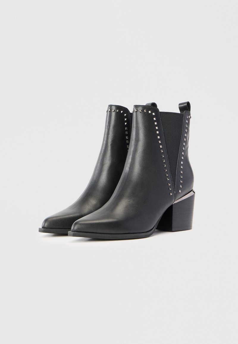 Schwarze Leder-Stiefeletten mit spitzem Zeh, Blockabsatz und Nietenverzierungen an den Seiten. Glatte Textur und elastische seitliche Einsätze.