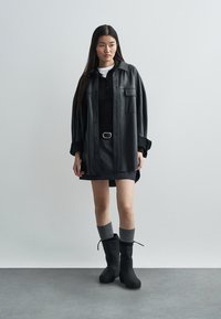 Czarna skórzana oversize koszula-kurtka, czarny polo top, jeansowa spódnica, szare wysokie skarpety do kolan i czarne botki na kostkę. Gładka tekstura, luźny krój.