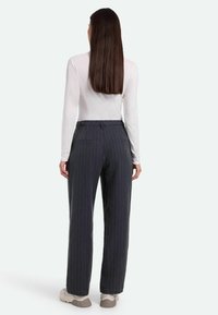 Graue schmal gestreifte Hosen mit einer lockeren Passform, ausgestattet mit seitlichen Taschen und einer glatten Textur. Getragen mit einem weißen Langarmhemd.