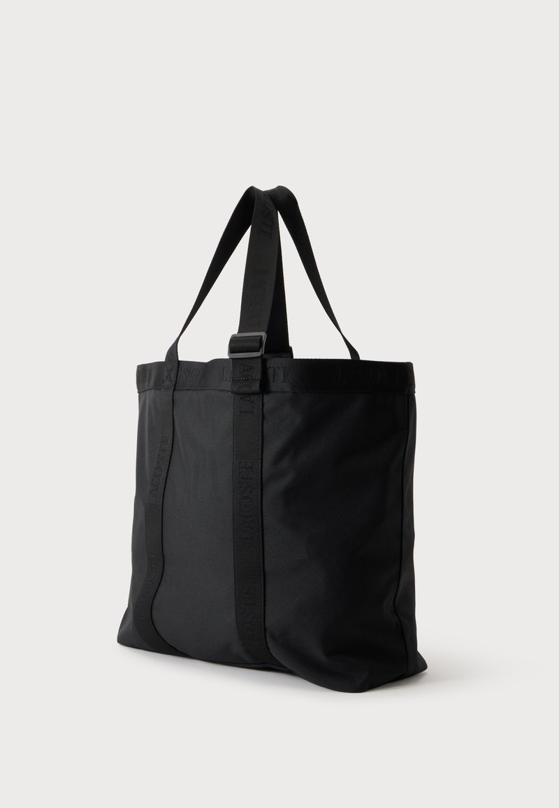 Borsa tote nera con due spallacci e una tracolla verticale con marchio in rilievo sottile su sfondo semplice.