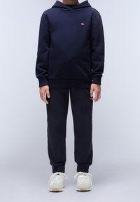 Felpa in misto cotone blu navy con tasca a marsupio e polsini a costine, abbinata a pantaloni jogging coordinati, completata da sneakers bianche e beige.