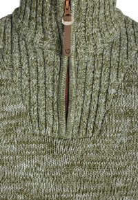 Jersey de punto con cuello alto en color verde oliva y blanco. Presenta una media cremallera con herrajes en tono beige y un patrón texturizado acanalado.