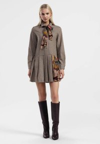 Abito a quadri marrone con maniche lunghe, scollo a fiocco e gonna plissettata; presenta un accento di motivo paisley colorato sull'orlo.