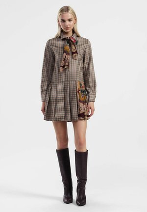 Abito a quadri marrone con maniche lunghe, scollo a fiocco e gonna plissettata; presenta un accento di motivo paisley colorato sull'orlo.