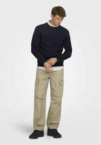Suéter marino con cuello redondo, pantalones cargo beiges y zapatillas negras. La tela parece suave con un acabado texturizado. Ajuste casual.