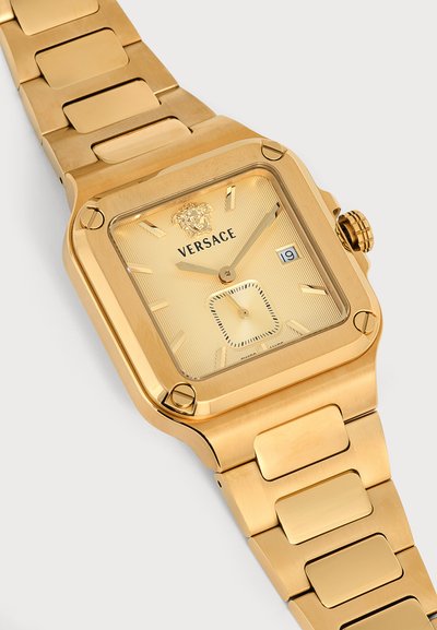 Montre-bracelet Versace dorée avec cadran carré, affichage de la date, logo Méduse en haut et bracelet à maillons métalliques.