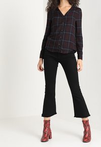 Sorte flared jeans kombineret med en mørkternet knap-op skjorte og røde støvler med slangeskindsprint og hæl. Skjorten har V-hals og lange ærmer.