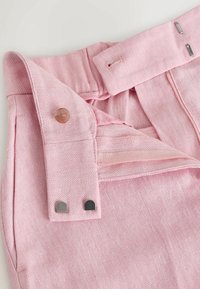 Roosa kangapükste vöökoha lähedal on nupp, peidetud tõmblukk ja topeltmetallist konksu- ning klambri kinnitused.