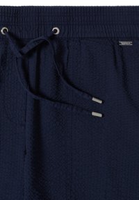 Gros plan sur un short en tissu texturé bleu marine avec taille élastique, poche avant et cordon avec embouts métalliques.