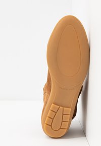 Bottine en daim couleur fauve avec une semelle en caoutchouc, présentant un motif texturé et un bout arrondi. Inscription "MADE IN SPAIN" visible sur la semelle.