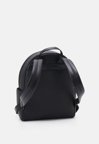 Mochila de cuero negro con una parte superior redondeada, superficie texturizada, correas ajustables y un pequeño asa en la parte superior para facilitar su transporte.