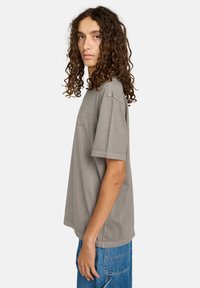 Szara bawełniana koszulka o luźnym kroju, z krótkimi rękawami i okrągłym dekoltem, w zestawieniu z niebieskimi dżinsami. Prosty, niezdobiony design.