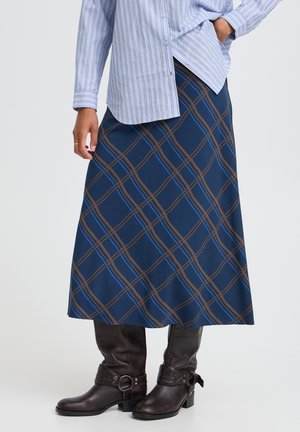 Personne portant une jupe midi à carreaux bleus, une chemise à rayures bleu clair boutonnée et des bottines marron foncé avec des détails de boucle.