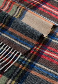 Soft wool scarf with multi-colored plaid patterns in red, blue, green, beige, and brown, featuring fringed ends and a folded corner.