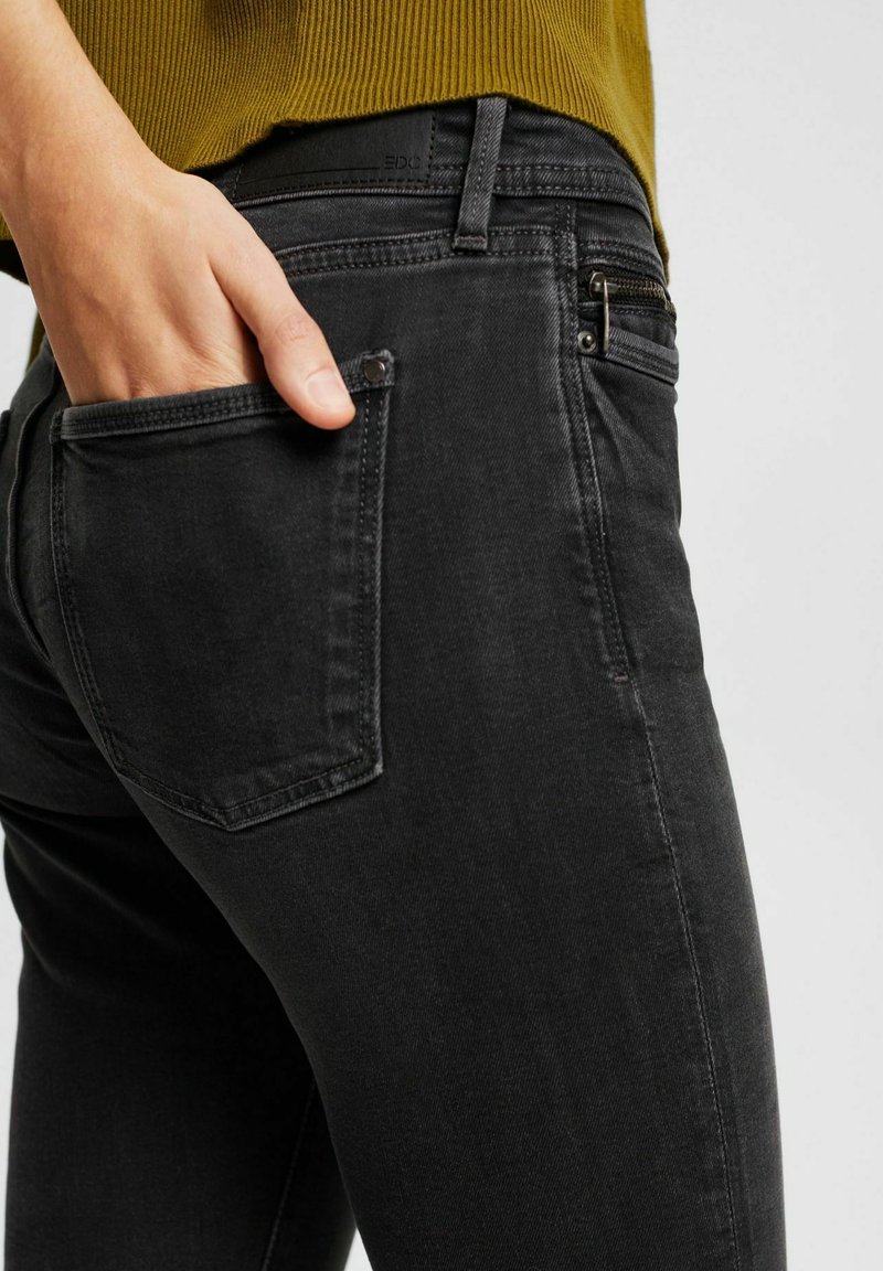 Jean en denim noir avec une coupe slim, un délavage subtil, une poche arrière inclinée et une poche zippée à l'avant. Tissu texturé.