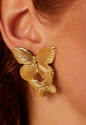 Gouden vlinderoorbellen met twee verschillende ontwerpen. De grotere vlinder heeft opvallende ribbeldetails, terwijl de kleinere een gladdere afwerking heeft.