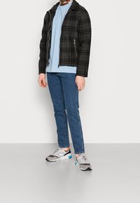 Svart och grå rutig jacka, ljusblå t-shirt, blå jeans och grå sneakers med färgglada detaljer. Dragkedja fram och designad krage.