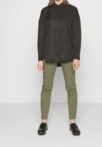 Black long-sleeve button-up shirt with a smooth texture, paired with olive green slim-fit pants and black clogs featuring metallic accents.