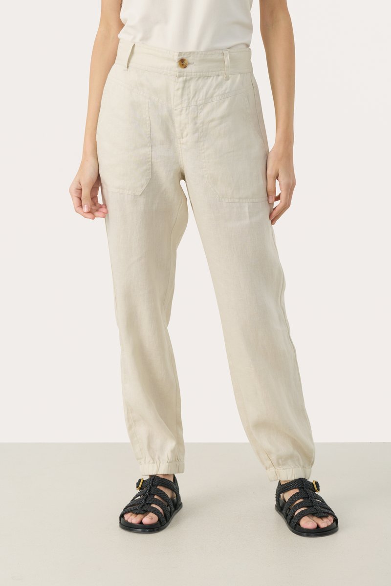 Light beige linen trousers with a relaxed fit, featuring side pockets and elastic cuffs, paired with strappy black sandals.