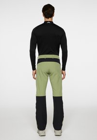 Musta pitkähihaine paita yhdistettynä vihreisiin ja mustiin väri-eroilla varustettuihin housuihin. Housuissa on kapea malli ja joustovyötärö, suunniteltu ulkokäyttöön.