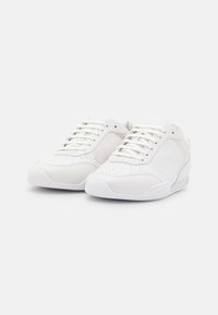 Valkoiset urheilukengät, joissa on sileä nahkapinta, reikäkärkikotelo, tasaiset nauhat ja kumipohja. Yksinkertainen ja siisti muotoilu.