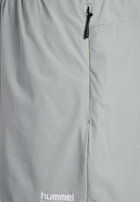 Jasnoszary materiał z pionowym szwem i czarnym suwakiem ze sznurkiem u góry, z białym logo "hummel" u dołu.