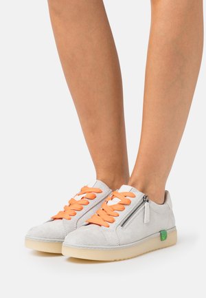Suede sneakers in light gray with orange laces, side zipper, and green logo accent. Features a textured sole and low-profile design.