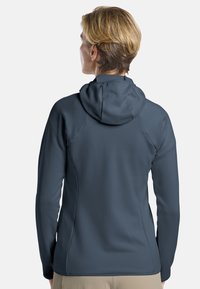 Veste à capuche en tissu gris foncé, avec un motif texturé, un design ajusté et des manches longues. La vue de dos montre une capuche ajustable.