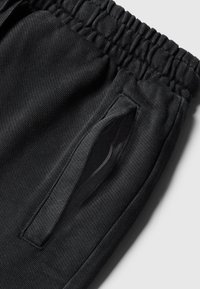 Zwarte joggings met gestructureerde stof, elastische tailleband en een zijrits zak. Het ontwerp benadrukt comfort en praktische toepasbaarheid.