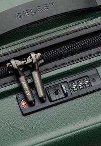 Valigia verde con finitura testurizzata, dotata di un sistema a doppia cerniera, etichette di sicurezza nere e un pannello con lucchetto combinato per una maggiore protezione.