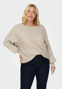 Light beige ribbed sweater with wide neckline and long sleeves, paired with dark blue jeans. Soft texture with a relaxed fit.