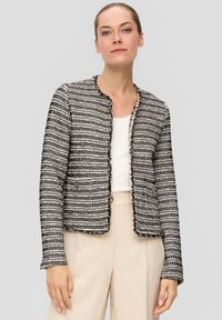 Mustvalge tweed jakk koos tekstuuriga mustriga, lühikese lõikega, ümmarguse kaelusega ja hõredate äärtega. Kombineeritud kerge tanktopiga.