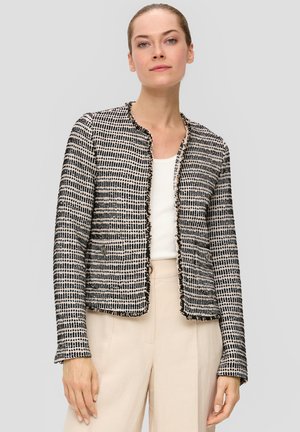 Musta-valkoinen tweed-takki, jossa on teksturoitu kuvio, lyhyt malli, pyöreä kaula-aukko ja röpelöiset reunat. Yhdistetty vaalean väriseen hihattomaan paitaan.