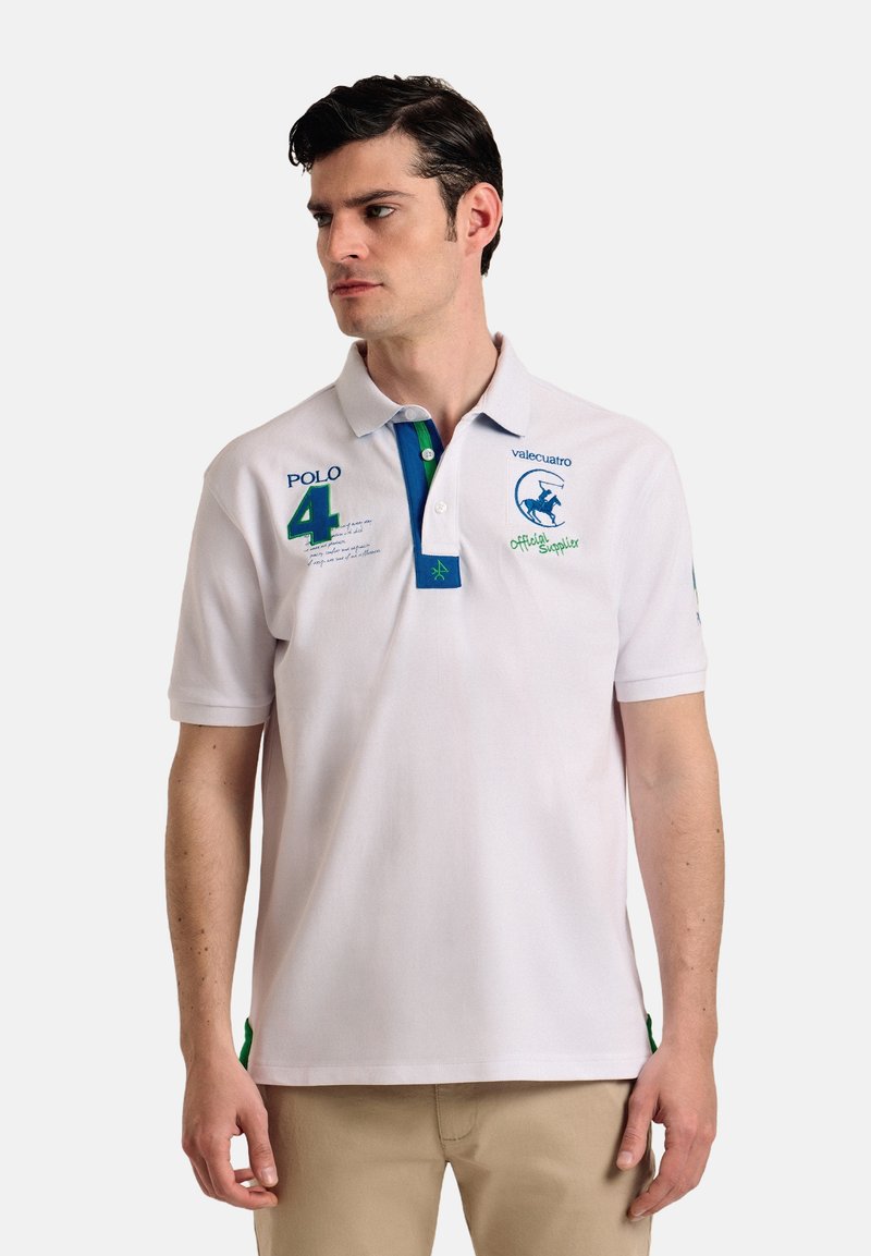 Camisa polo blanca de manga corta, con acentos en azul y verde, logos bordados y texto, que cuenta con un cuello con dos botones y aberturas en los laterales.