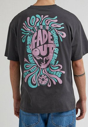 Dos d'un T-shirt noir avec un design abstrait coloré violet et turquoise d'un visage, accompagné du texte "Fade Out" et "Into all the different shades of blue."