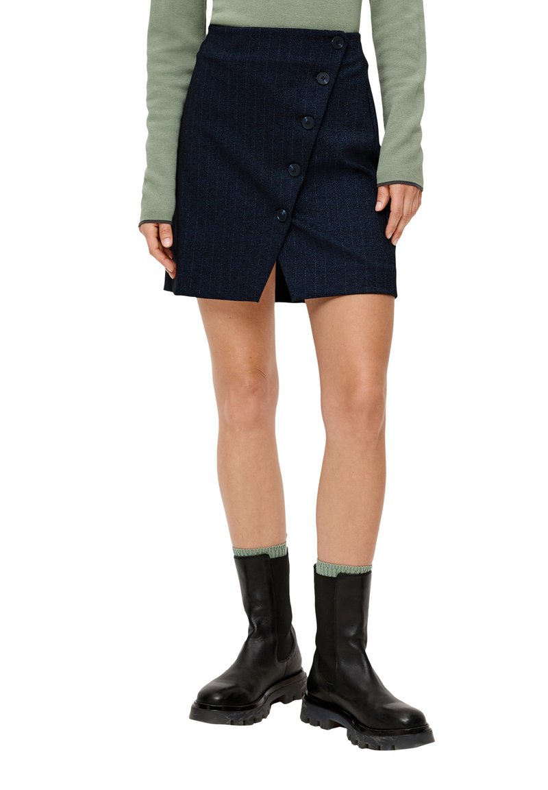 Dunkelblaue, gestreifte Minirock mit einem Schlitz vorne und fünf schwarzen Knöpfen. Kombiniert mit einem grünen, langärmligen Oberteil und schwarzen Stiefeletten.