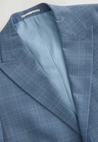 Blaues kariertes Sakkos mit einer strukturierten Außenseite und glattem hellblauem Innenfutter. Zu den bemerkenswerten Merkmalen gehören ein spitz zulaufender Revers und gestochen genähte Akzente.