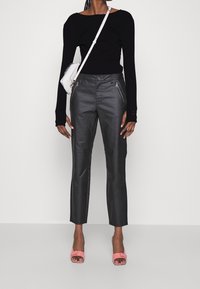 Woman wearing a black long-sleeve top, black high-waist pants with zipper pockets, white crossbody bag, and pink open-toe heels.