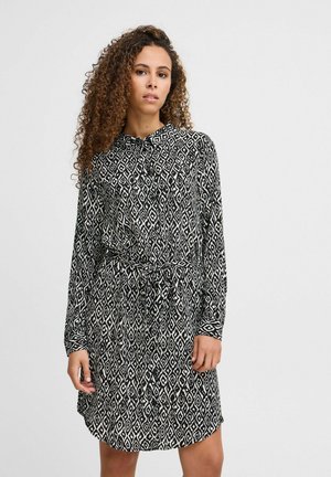 Musta ja valkoinen kuviollinen mekko, jossa on pitkät hihat, kaulus ja sidottu vyötärö. Mekossa on timanttikuosiset ja pehmeä kangas.