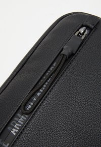 Borsa nera in pelle texture con chiusura a zip, dotata di un cordino intrecciato e una fodera interna stampata.