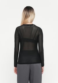 Black long-sleeve top made from sheer fabric, featuring a round neckline and smooth texture. Worn with gray trousers.